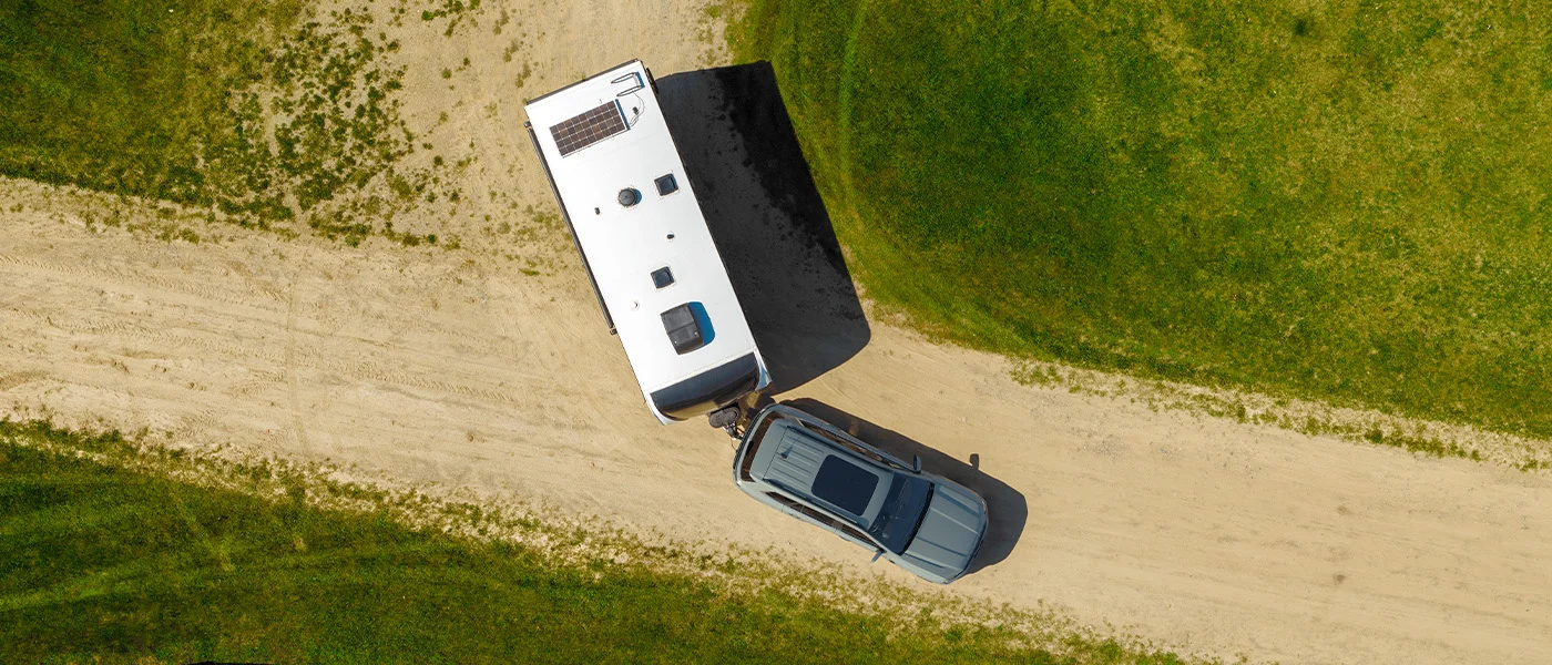 An Everest seen from above towing a caravan along a curved gravel road through farmland