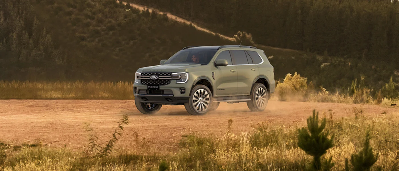 A grey-green Ford Everest kicking up dust across golden tussock country