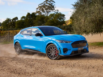 A grabber blue Mustang Mach-E electric SUV on a dusty vineyard road