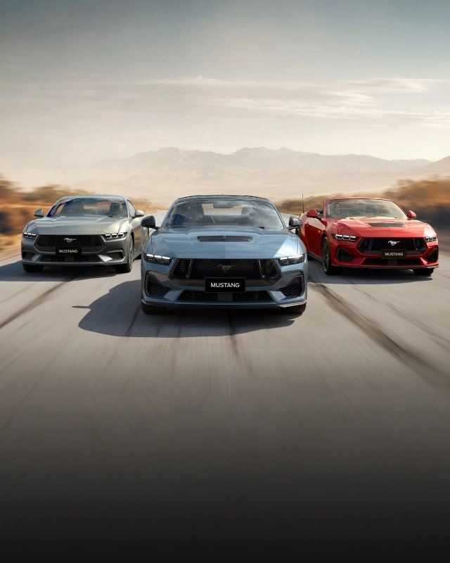 Three seventh-generation Ford Mustangs charging along a desert highway at dusk