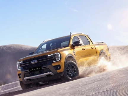 A luxe yellow Ford Ranger Wildtrak drifting on a gravel road, dust trailing