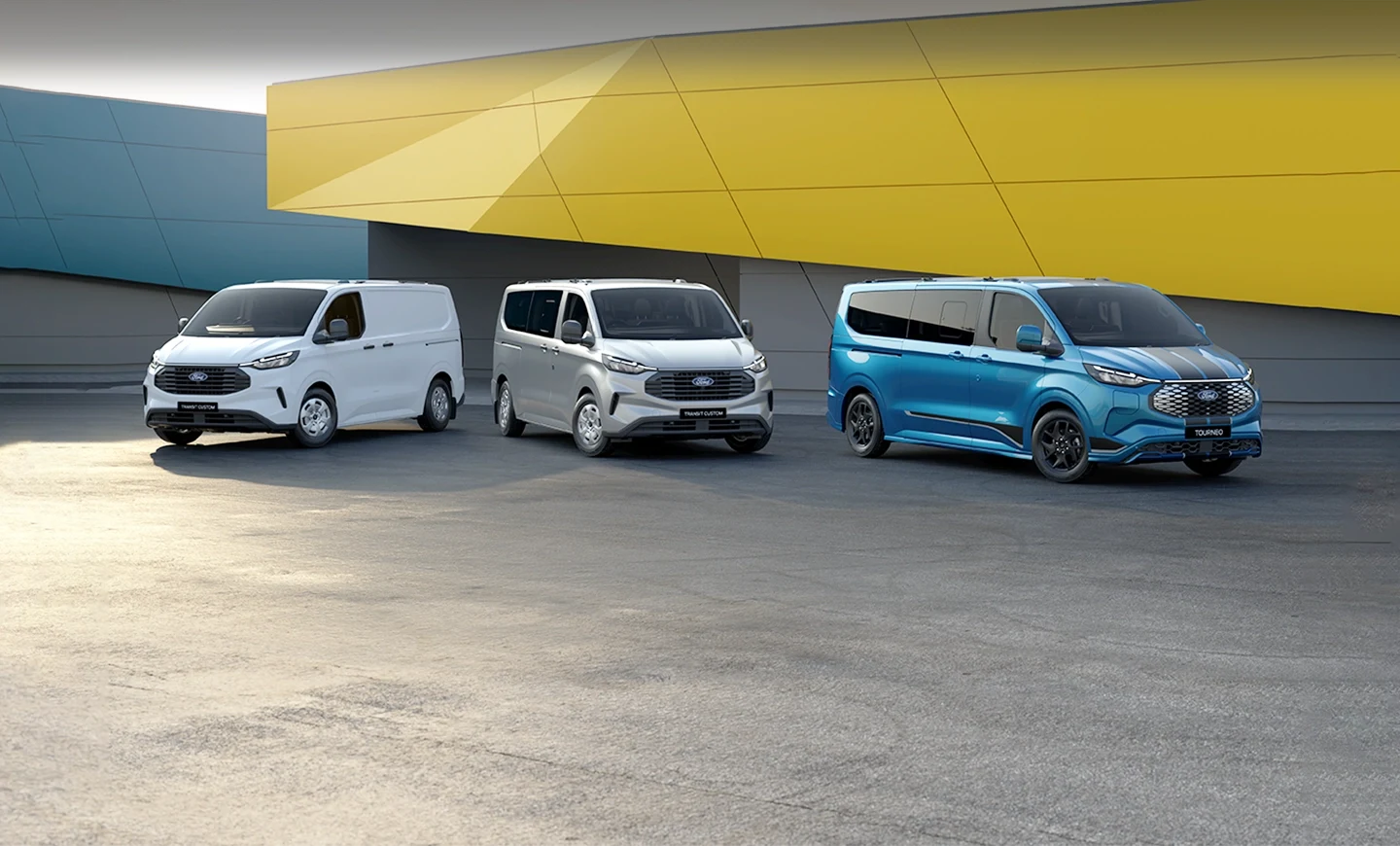 Transit Custom Van, Kombi and Tourneo parked in front of a yellow and blue warehouse